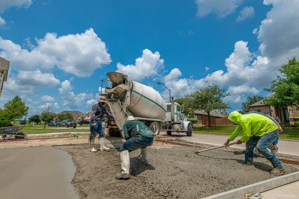 Construction workers laying concrete for a driveway in Fort Worth, Texas, under a bright blue sky.